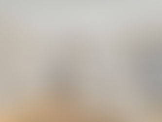 Modern kitchen with beige cabinets, stainless steel appliances, an island with a gold faucet, and pendant lights, featuring natural light.