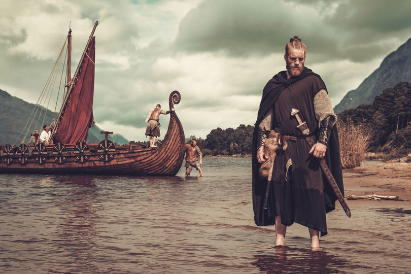 Viking warrior with sword standing near Drakkar on the seashore..jpg