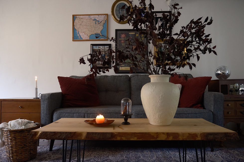 Cozy living room with grey sofa, red cushions, large vase with branches, candlelit wooden table. Wall art includes a U.S. map.