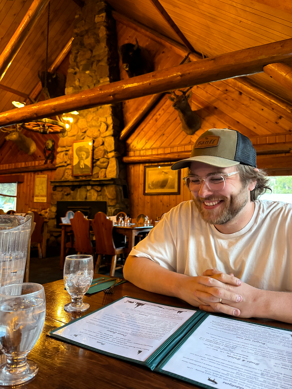 a man smiles at a table in a restaurant that has wooden beams and a stone fireplace
