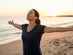 Mulher saudável e feliz a respirar ar puro numa praia ao amanhecer, representando a liberdade conquistada com a Fumava e o questionamento sobre o viver sem fumo preço