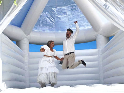 A couple joyfully jumps in an inflatable castle, showcasing their happiness and playful spirit in a colourful environment.