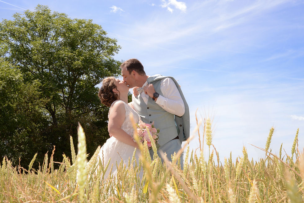 Baiser passionné d'un couple de mariés au milieu d'un champ de blé doré sous un ciel bleu en Bourgogne.