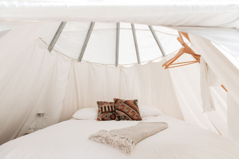 Interior view of a glamping tepee with cozy bedding, soft linens, and warm lighting.