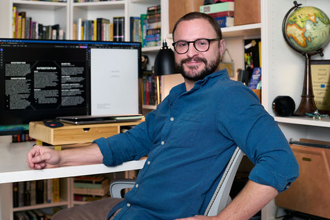 Horizontal portrait of Christian Rousseau sitting at his desk wearing a blue shirt, photographed by Hart Getzen Photography