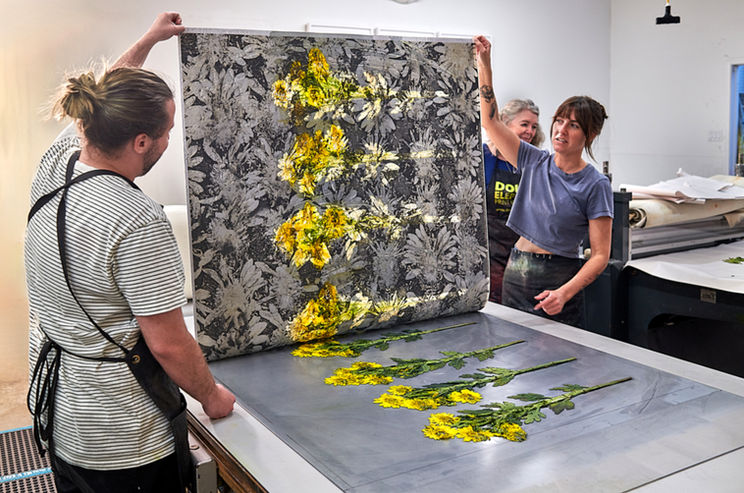 Artists holding large floral print above metal plate