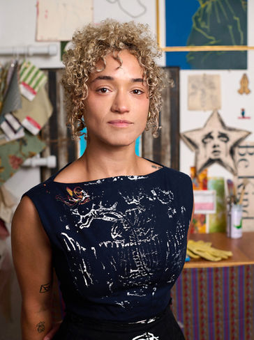 Austin artist Allie Gallion standing in her studio dressed in a black dress she printed.