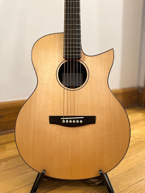 A guitar with a Florentine cutaway, sitka spruce top, ebony bridge and unbleached bone saddle and bridge pins sitting on a guitar stand. 