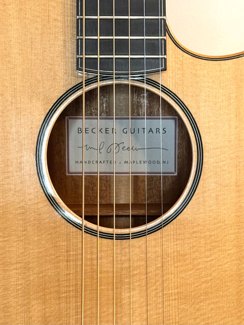 The face of a Sitka Spruce guitar.  The rosette is thin white and black purfling lines and the maker's label is glued onto the inside of the back centered on the Rosette.