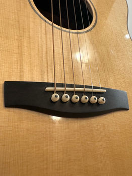The ebony bridge of the guitar with a satin finish, polished unbleached bone saddle and bridge pins. 