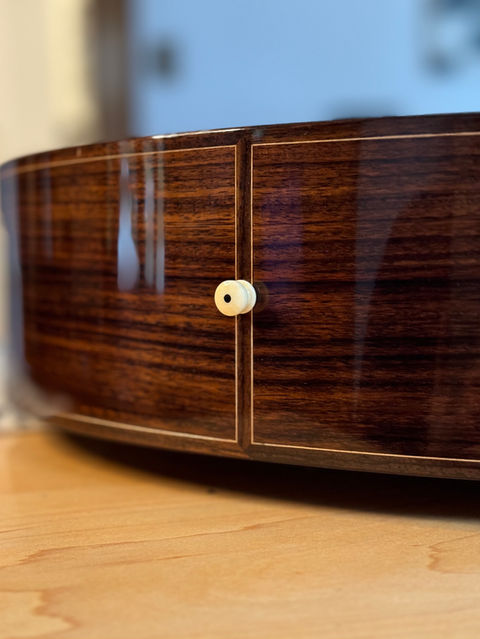 The end-wedge of an East Indian Rosewood guitar with matching rosewood binding, maple purfling, and an unbleached bone end pin.