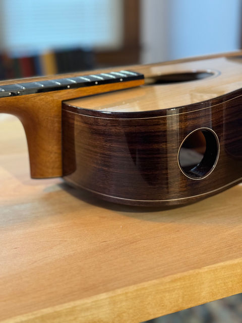 A newly finished upper bout of an East Indian Rosewood guitar with a circular opening in the bass side upper bout.  The opening is bound in matching Rosewood and has a thin line of maple purfling.  The fretboard extension of the guitar floats over the guitar top by 3 millimeters. 
