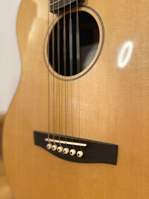 The face of a Sitka Spruce guitar with an Ebony bridge and unbleached bone bridge pins.