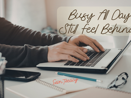 Hands typing on a laptop with notebooks and glasses on a desk. Text reads "Busy All Day, Still Feel Behind?". Erin Treacy Coaching logo.