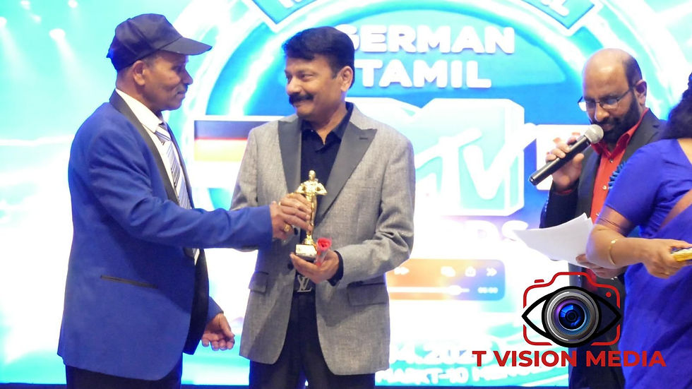 Ravi Atchuthan receives the award trophy on stage, sharing a celebratory moment with presenters at the 34th International Germany Tamil MTV Awards.