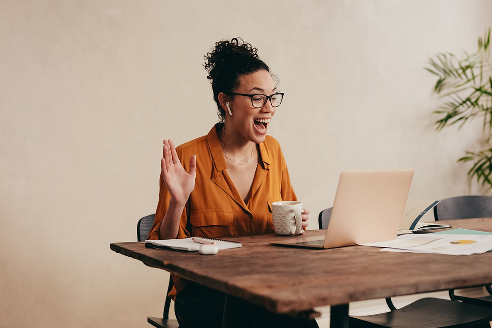 Mujer feliz usando sus AirPods mientras saluda a su computadora portátil
