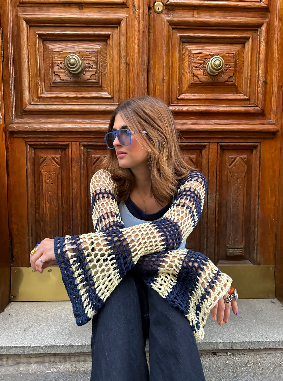 Modelo con gafas de sol sentada en un portal con el bolero knit Lemon Coast de THE NODO