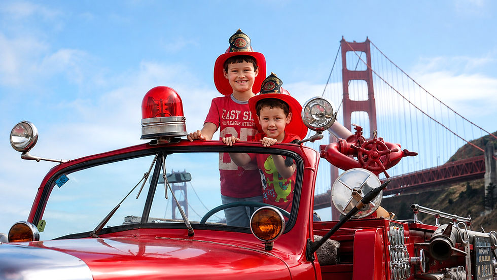Two children wearing firefighter helmets aboard the vintage Mack fire engine