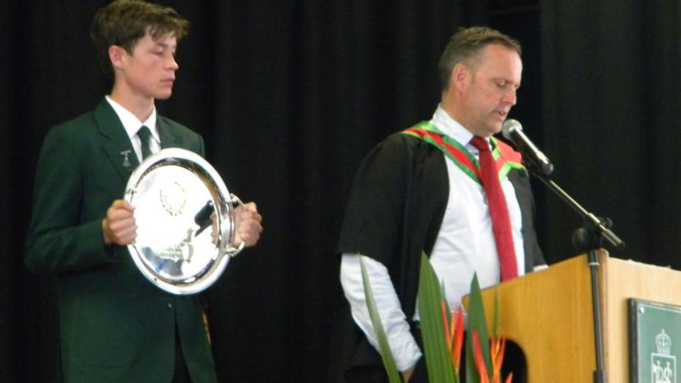 Paul Rushworth-Brown addressing a group of students during a school presentation while holding a commemorative plate.