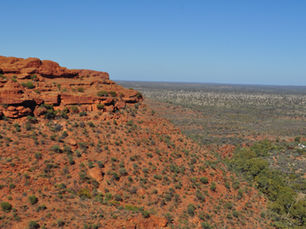 Wide inland landscape in central Australia, showing rocky escarpments and sparse vegetation under an open sky.
