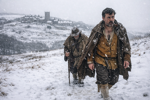 Two exhausted men in seventeenth-century clothing walking through heavy snow toward a distant Yorkshire village during winter