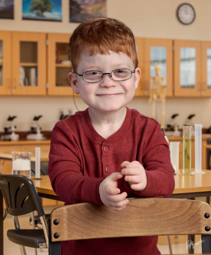 Donovan smiles for a school picture, wearing a red shirt and glasses and sporting his characteristic red hair.