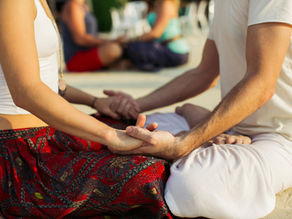 Ein Paar sitzt sich im Schneidersitz gegenüber und hält sich die Hände – achtsame Vorbereitung auf die Übung „Begegnung der Herzen“, bei der die Hände auf den Herzraum des Partners gelegt werden.