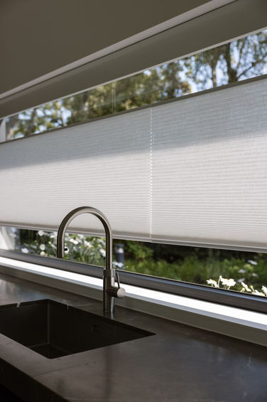 Kjøkken med vask og vindu, med hvite Plissegardiner for solskjerming.