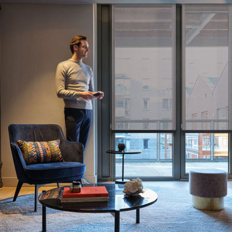 Mann som står i stuen og styrer rullegardiner med fjernkontroll