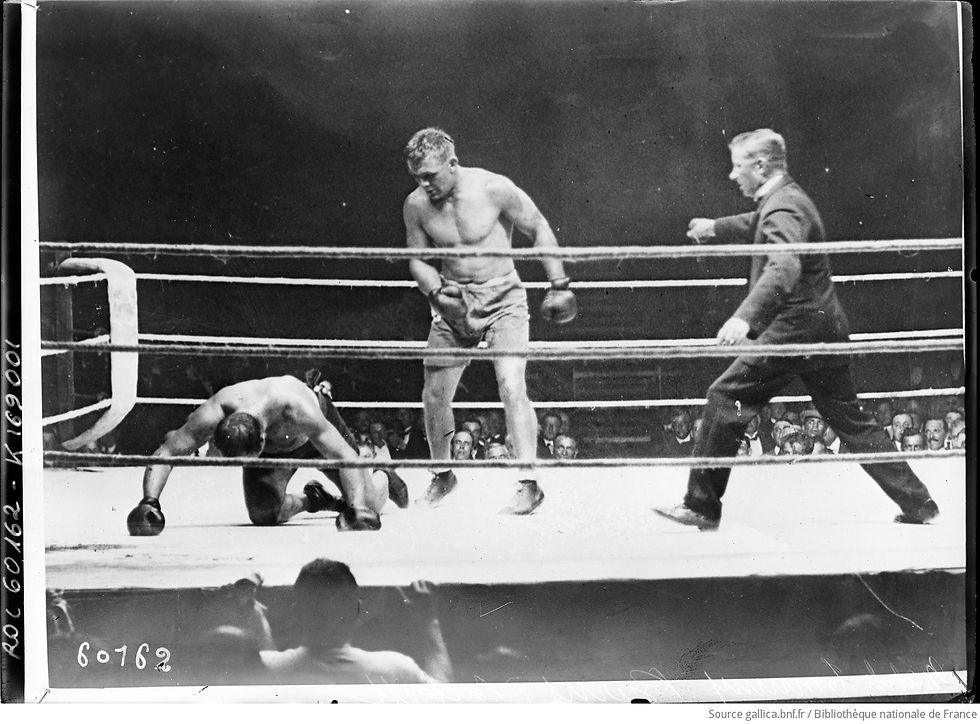 Zwart-wit persfoto uit 1920 van een boksring waarin Joe Beckett die naar voren komt met een stoot en Tommy Burns hard in zijn gezicht raakt