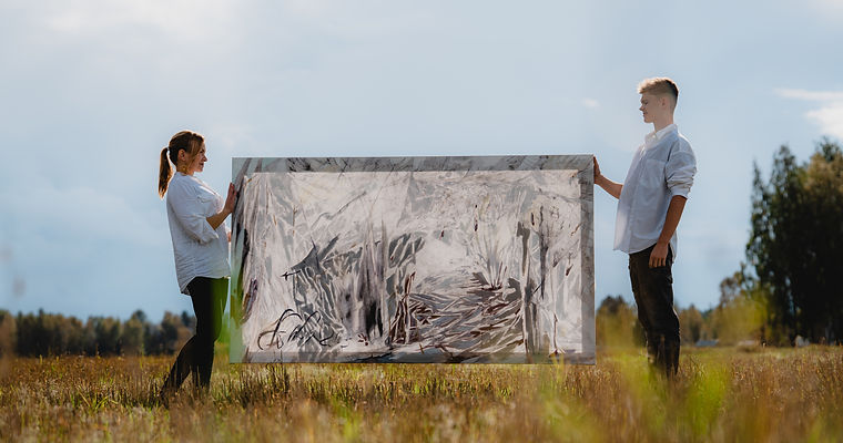 Two young people holding a large abstract painting in a field.