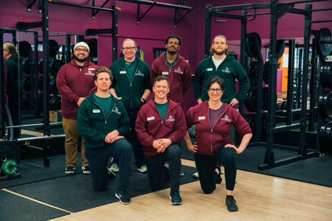 The full Ampersand Fitness personal training team posing inside the gym, wearing branded hoodies and smiling