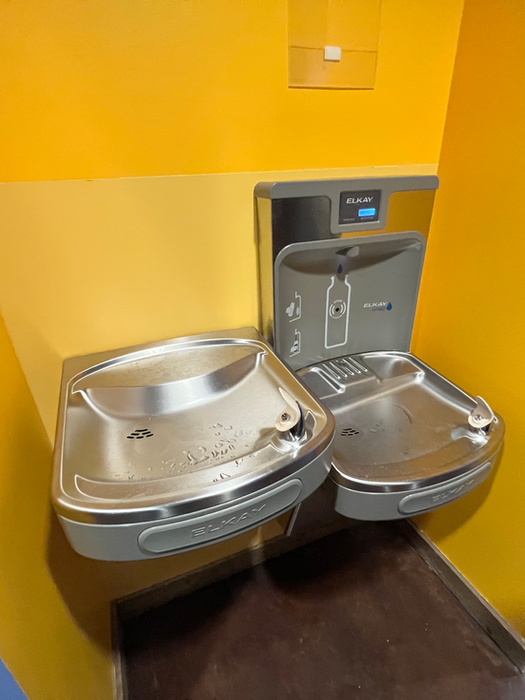 Hydration station at Ampersand Fitness with dual Elkay water fountains and a bottle filler against a yellow wall
