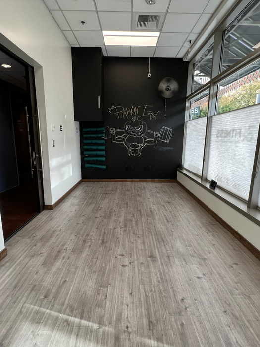 Private studio room at Ampersand Fitness with wood flooring, natural light, and a chalkboard wall for personal training or stretching.