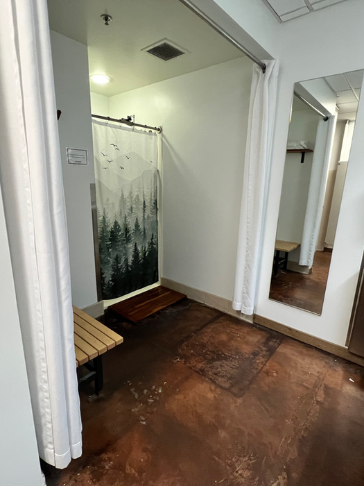 Private shower area at Ampersand Fitness with curtain dividers, towel service, sink counter, mirror, and sanitation amenities