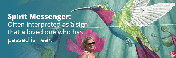 Hummingbird mural with Linda standing in front of it, with text over the image that says "Spirit Messenger: Often interpreted as a sign that a loved one who has passed is near."