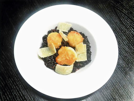 Drei gebratene Jakobsmuscheln liegen auf schwarzem Reis.