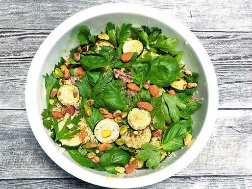 Eine Schüssel voller Salat mit gebratenen Zucchini-Scheiben, Nüssen und viel Grün.