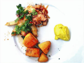 Oktopus mit Bratkartoffeln und Spargel auf einem Teller.