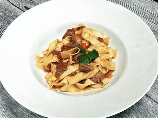 Ein Teller mit breiten Nudeln, die mit Entenragout vermischt sind.