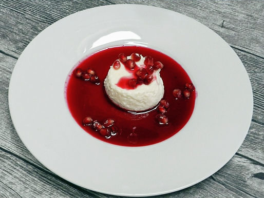 Ein weißen Joghurt-Rictta-Törtchen umgeben von roter Granatapfelsauce.Granat