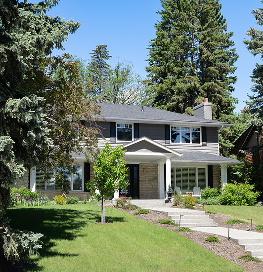 1970's style home with large windows, steps to front door under a canopy with a manicured lawn and florals in summer