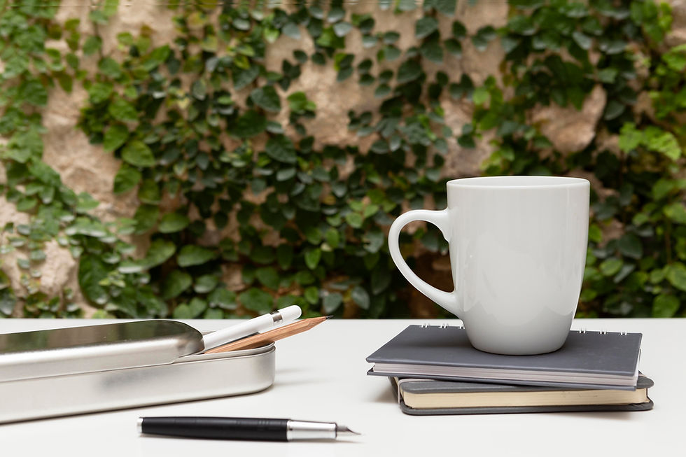 A wall with a climbing vine, a set of pencils and notebooks with a white mug on top to depict productivity in a natural office setting.