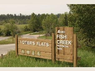 Votier's Flats Sign at the entrance to Fish Creek Provincial Park. It is summer with a wildfire smoke haze in the sky.