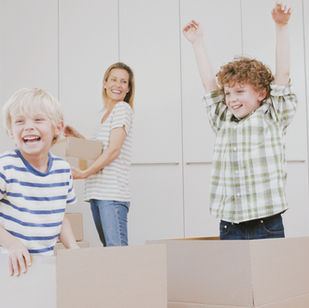 Two boys playing in moving boxes with mom watching in the background in a minimalistic home