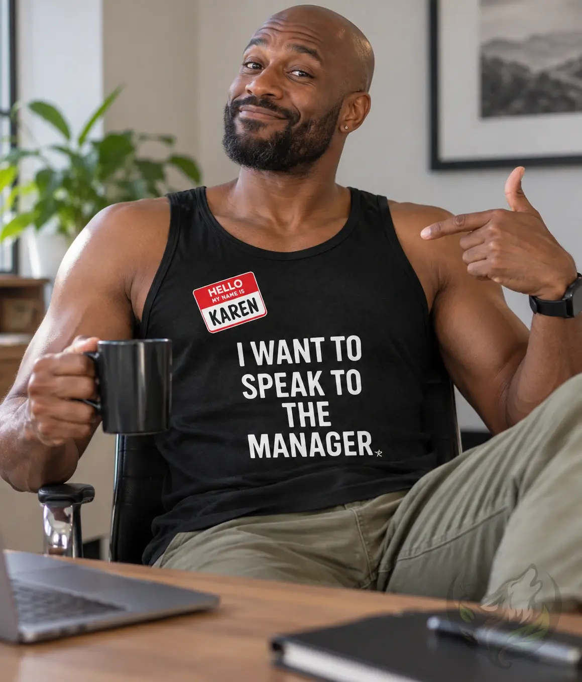 Man wearing a black Speak to the Manager tank top while pointing at the design and holding a mug