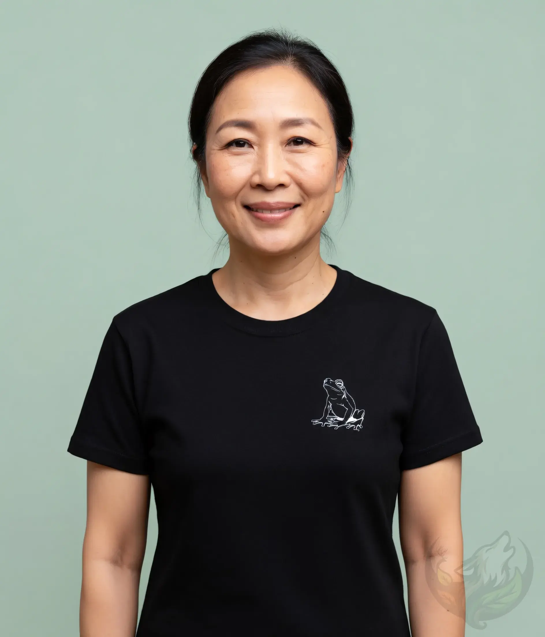 Smiling older Asian woman wearing a black fitted t-shirt with a delicate minimalist frog line art on the left chest.