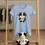 Thumbnail: Light blue fitted tee with Cute Cow Vegan Life design hanging on a wooden rack with a matching cow plush below.