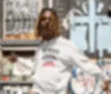 Man wearing white unisex hoodie with The World Doesn't Need Weapons It Needs Hearts design outdoors