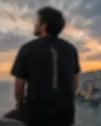 Man overlooking ocean sunset wearing black unisex shirt with moon quote design on the back